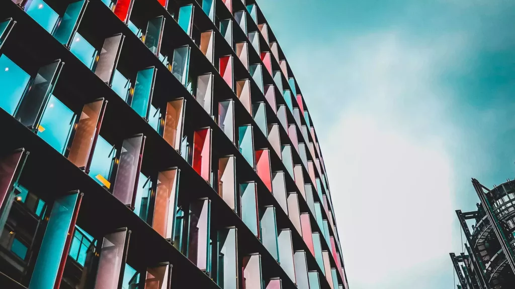 Side of building covered in windows, with shades of blues and oranges. Image by Joshua Fuller Unsplash