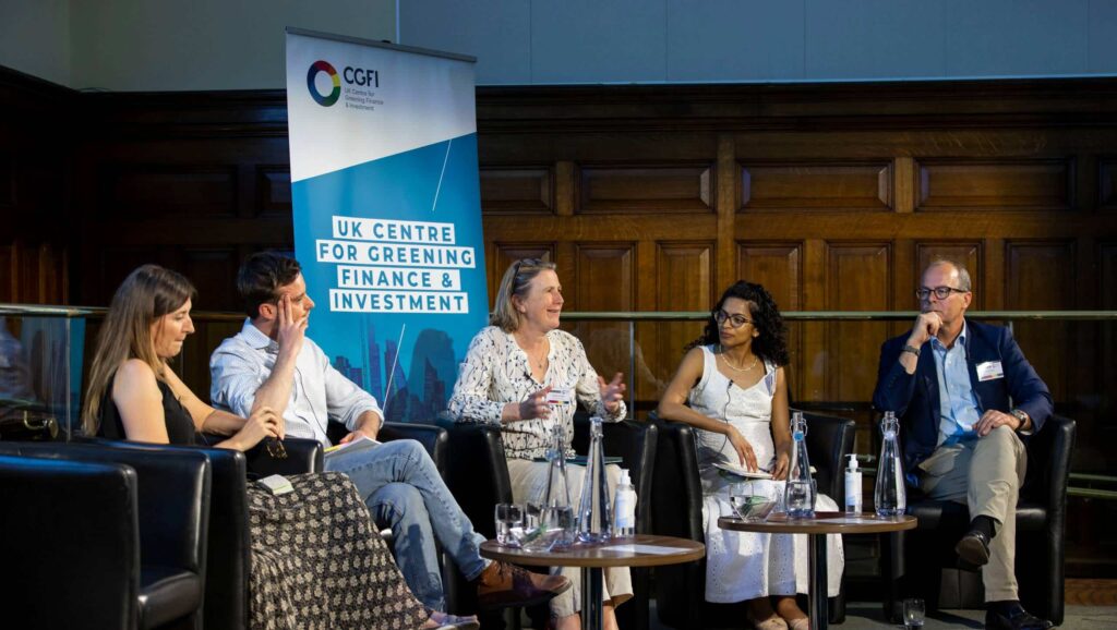 3 women and 2 men sat on a stage with small tables in front of them. A panel at the CGFI forum